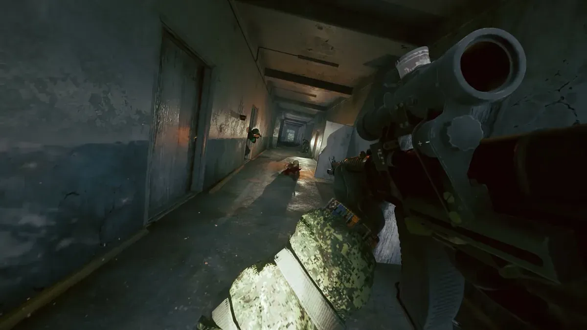 An operative moving down a dim concrete corridor with a rifle raised